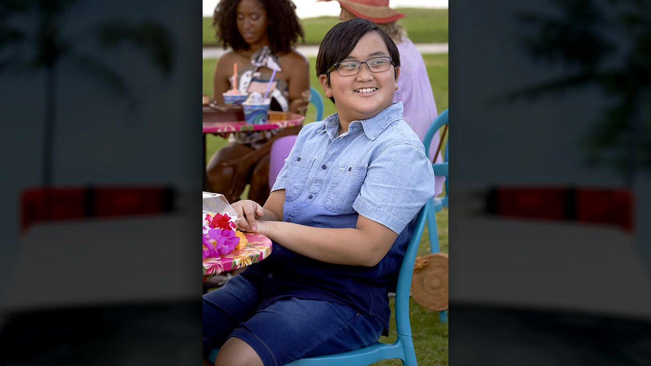 Wes Tian as “Brian Patrick Kamealoha” smiling while sitting down at a table during the day. From the Disney+ Original series Doogie Kamealoha, M.D.