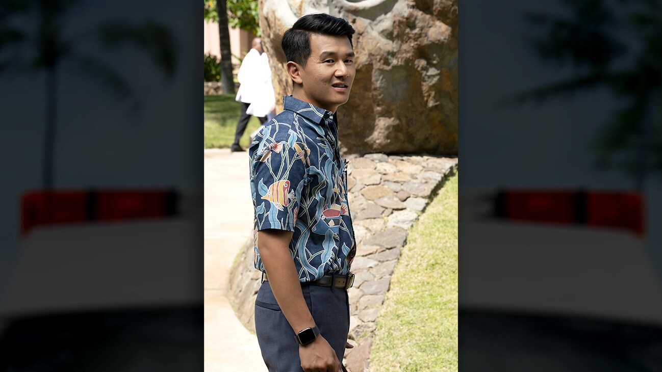 Ronny Chieng as “Dr. Lee” standing on a walkway near grass during the day. From the Disney+ Original series Doogie Kamealoha, M.D.
