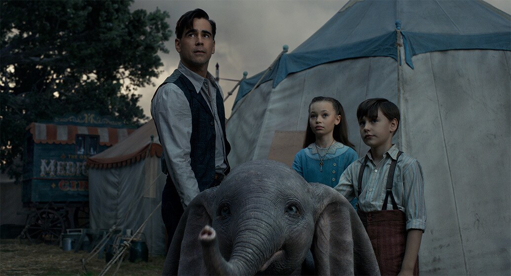 Colin Farrell (Holt Farrier), Nico Parker (Milly Farrier) and Finley Hobbins (Joe Farrier) stand behind Dumbo from the movie "Dumbo"