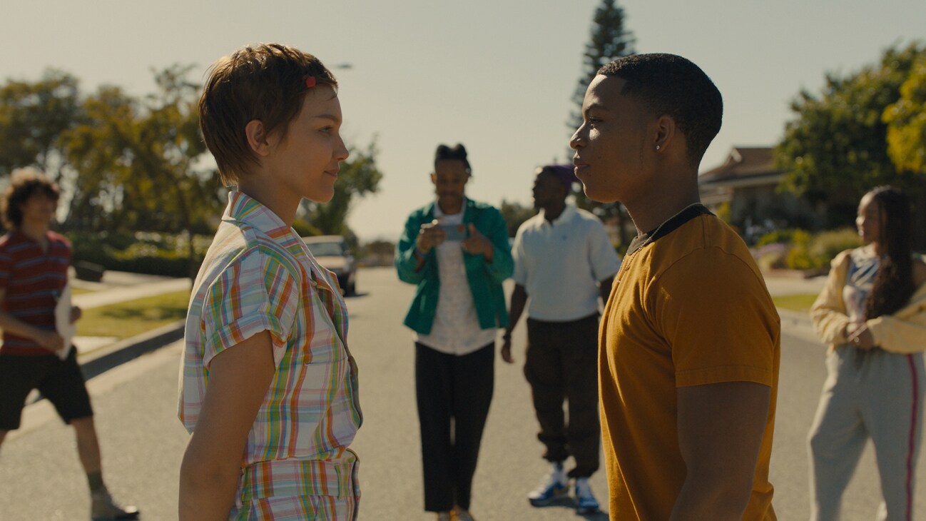 Hollywood Stargirl | First Look Photo | Image of Stargirl Caraway (actor Grace VanderWaal) and Evan (Elijah Richardson) standing across from each other in a scene, as Terrell (Tyrel Jackson Williams) and crew film them.