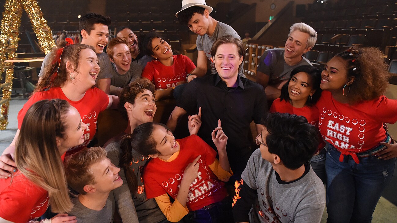 Lucas Grabeel (actor Lucas Grabeel) standing in the middle of the cast from the Disney+ Original series "High School Musical: The Musical: The Series".