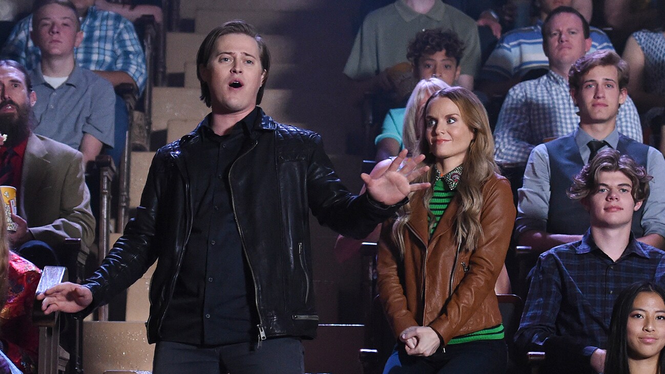 Miss Jenn (actor Kate Reinders) and Lucas Grabeel (actor Lucas Grabeel) standing in the audience from the Disney+ Original series "High School Musical: The Musical: The Series".