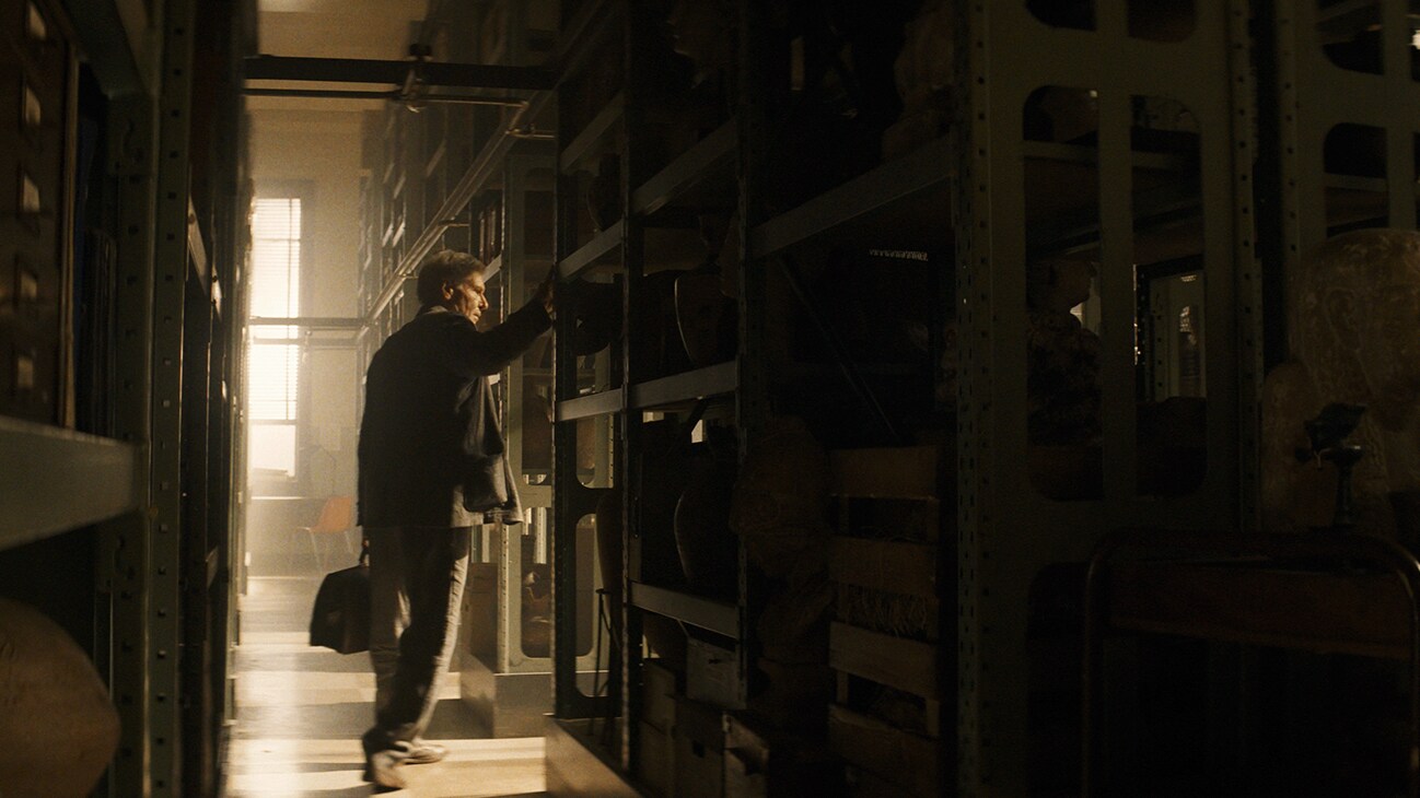 Indiana Jones (actor Harrison Ford) standing between rows of shelves from the Disney movie, "Indiana Jones and the Dial of Destiny."