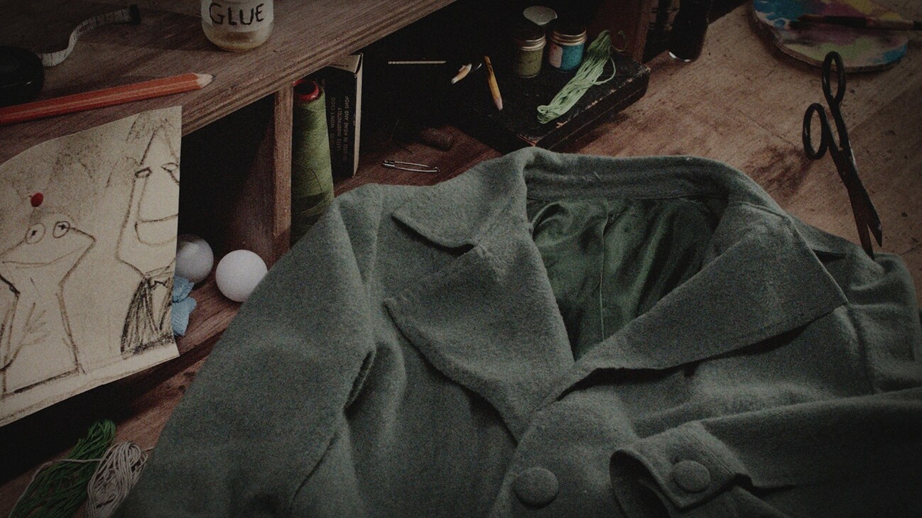 Image of a coat and a drawing on a workbench from the Disney+ Original documentary, "Jim Henson Idea Man."