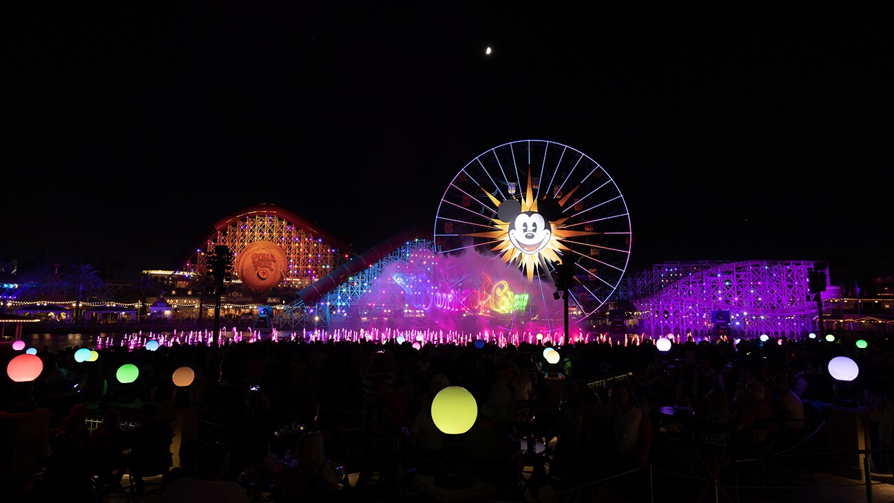 Nightime image of Disney California Adventure's World of Color performance with the Mickey ferris wheel and roller coaster lit in the background.