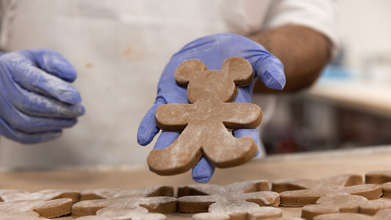 Image of a cast member holding a gingerbread cookie shaped like Mickey Mouse.