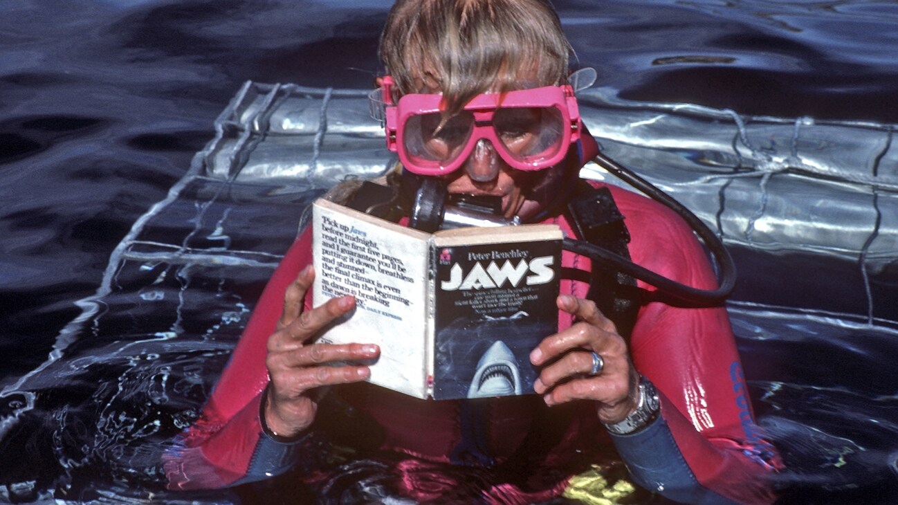 Valerie Taylor in scuba gear reading the Jaws book on top a shark cage in 1982. (photo credit: Ron & Valerie Taylor)