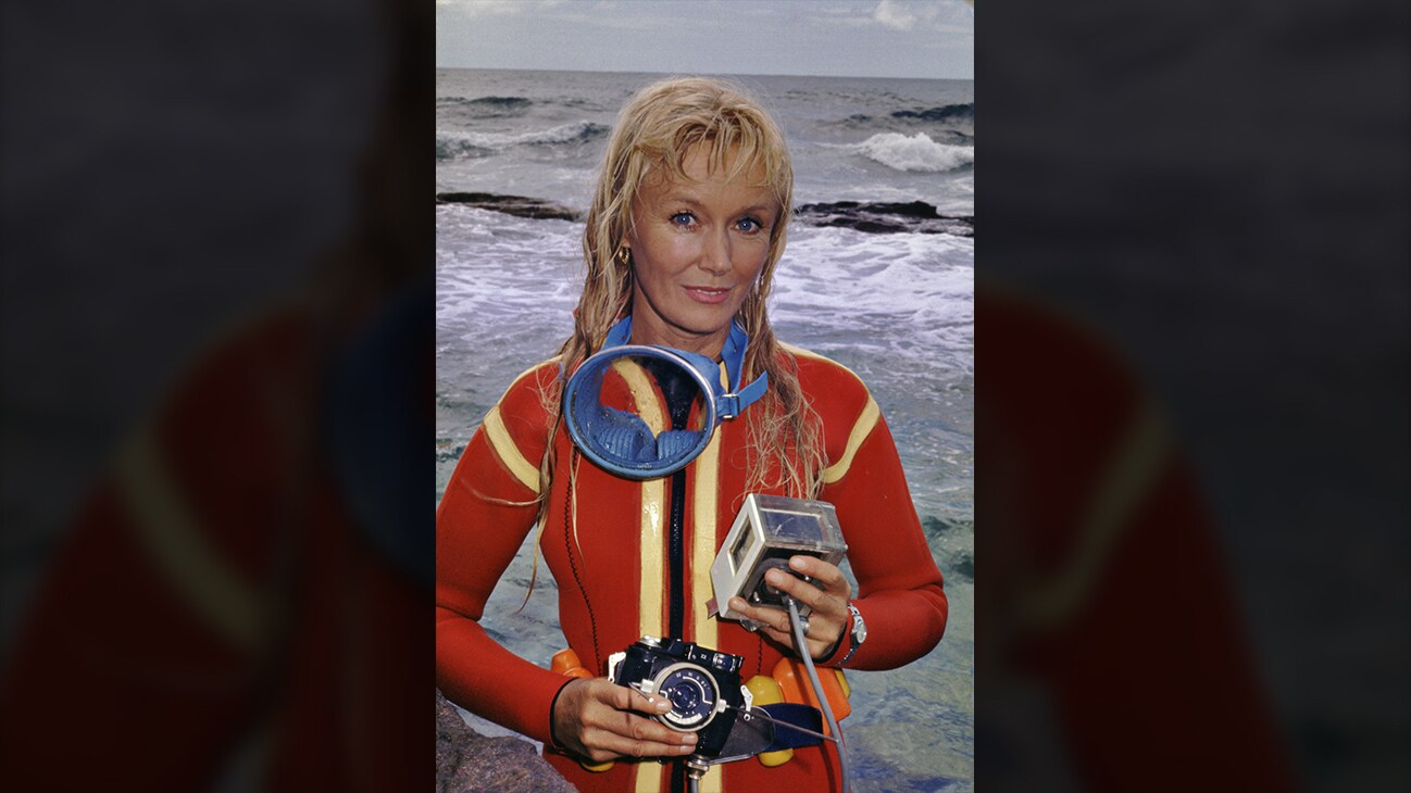 Valerie Taylor in red wetsuit posing with camera equipment. (photo credit: Ron & Valerie Taylor)