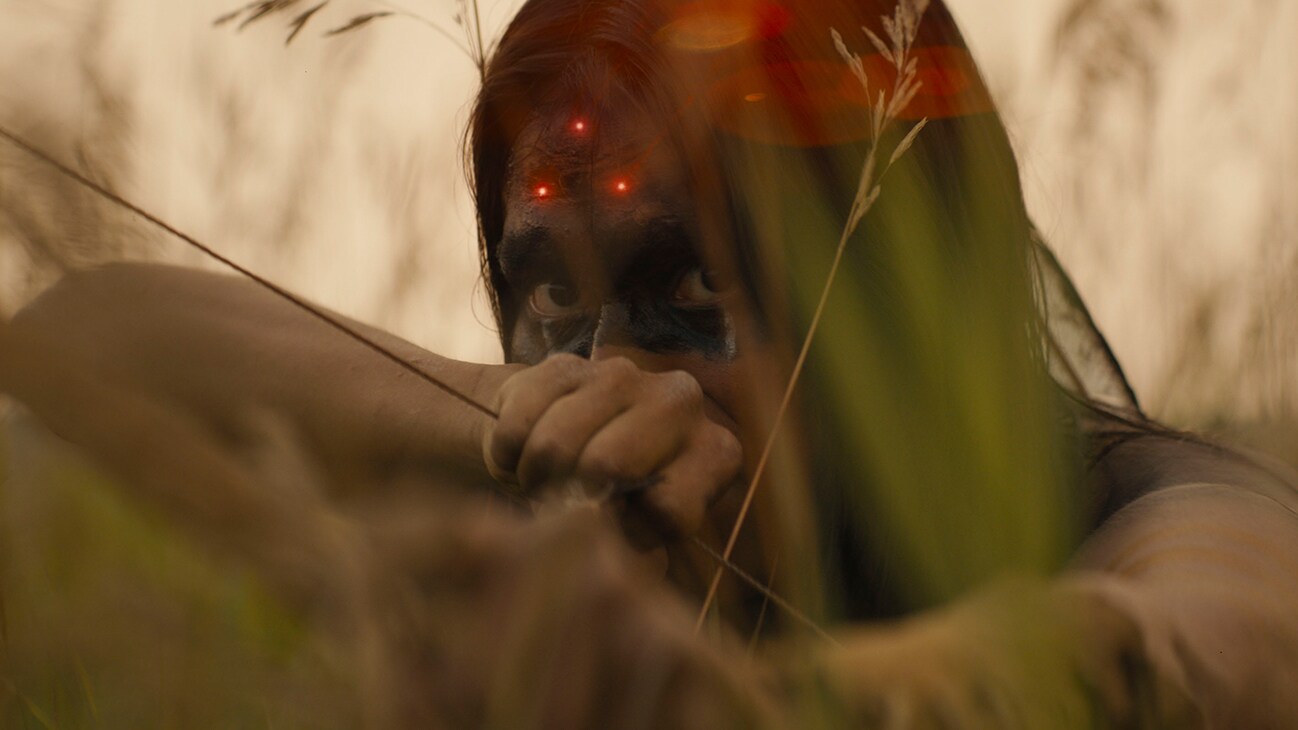 Image of a Native American with a bow drawn and a red laser sight on their forehead from the movie, "Prey".