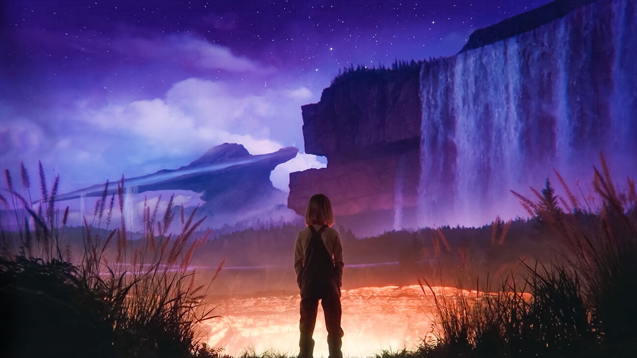 Image of a young person in front of a large waterfall with a strange rock formation in the background from the Disney+ movie, "Remembering".