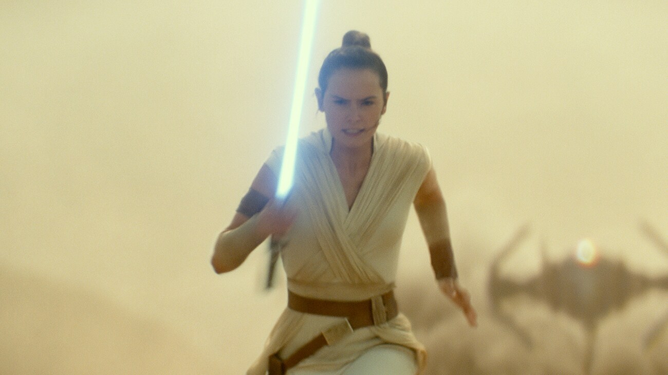 Daisy Ridley as Rey running with her light saber in hand and a ship in the back in "Star Wars: The Rise of Skywalker"