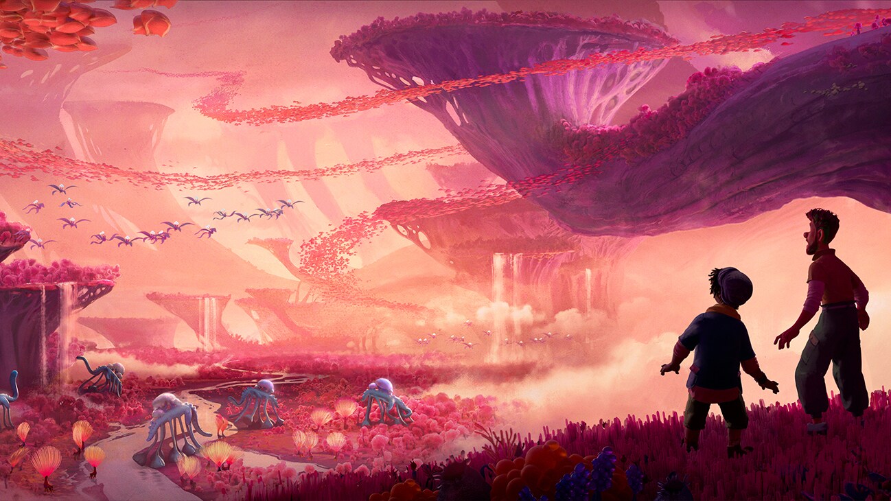 (L-R) Ethan Clade (voiced by Jaboukie Young-White) and Searcher Clade (voiced by Jake Gyllenhaal) stand on a hill, looking towards a valley filled with giant roaming creatures, plants, and flying creatures.