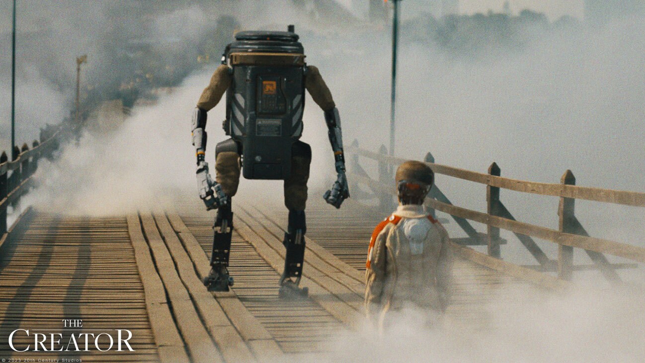 Image of a biped robot and small human staring at each other on a bridge from the 20th Century Studios movie, "The Creator." 