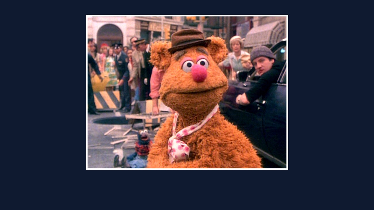 Fozzie standing next to a car in the street from the Disney movie The Great Muppet Caper.