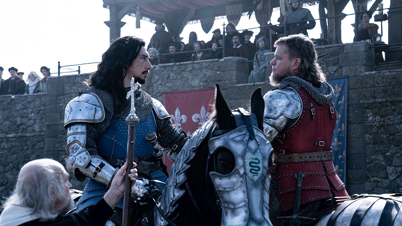 Jacques Le Gris (actor Adam Driver) and Jean de Carrouges (actor Matt Damon) in medival armor starting at each other on horseback in front of a stand from the 20th Century Studios movie The Last Duel.