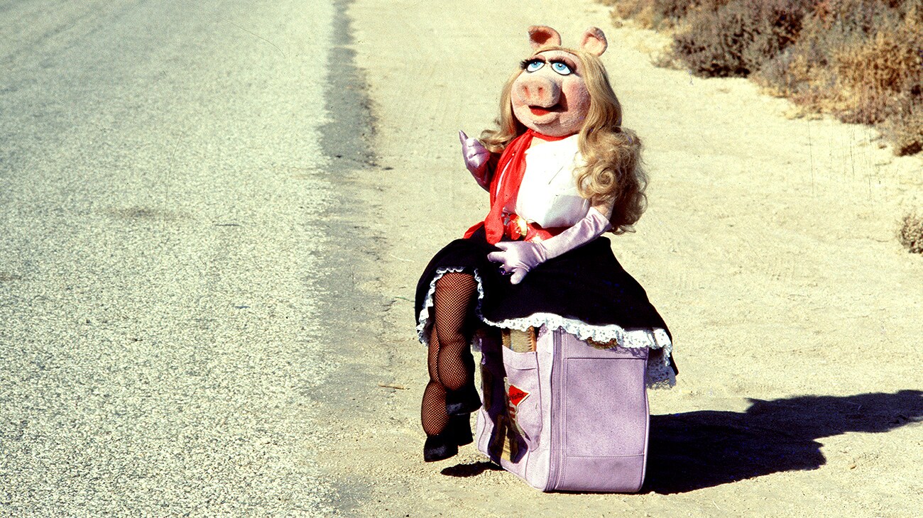 Miss Piggy sitting on a suitcase by the side of a road in The Muppet Movie