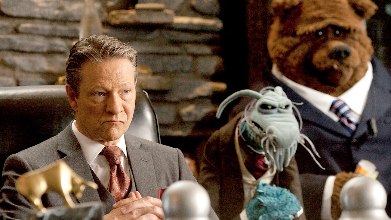 Chris Cooper as Tex Richman with sinister looking muppets at a desk