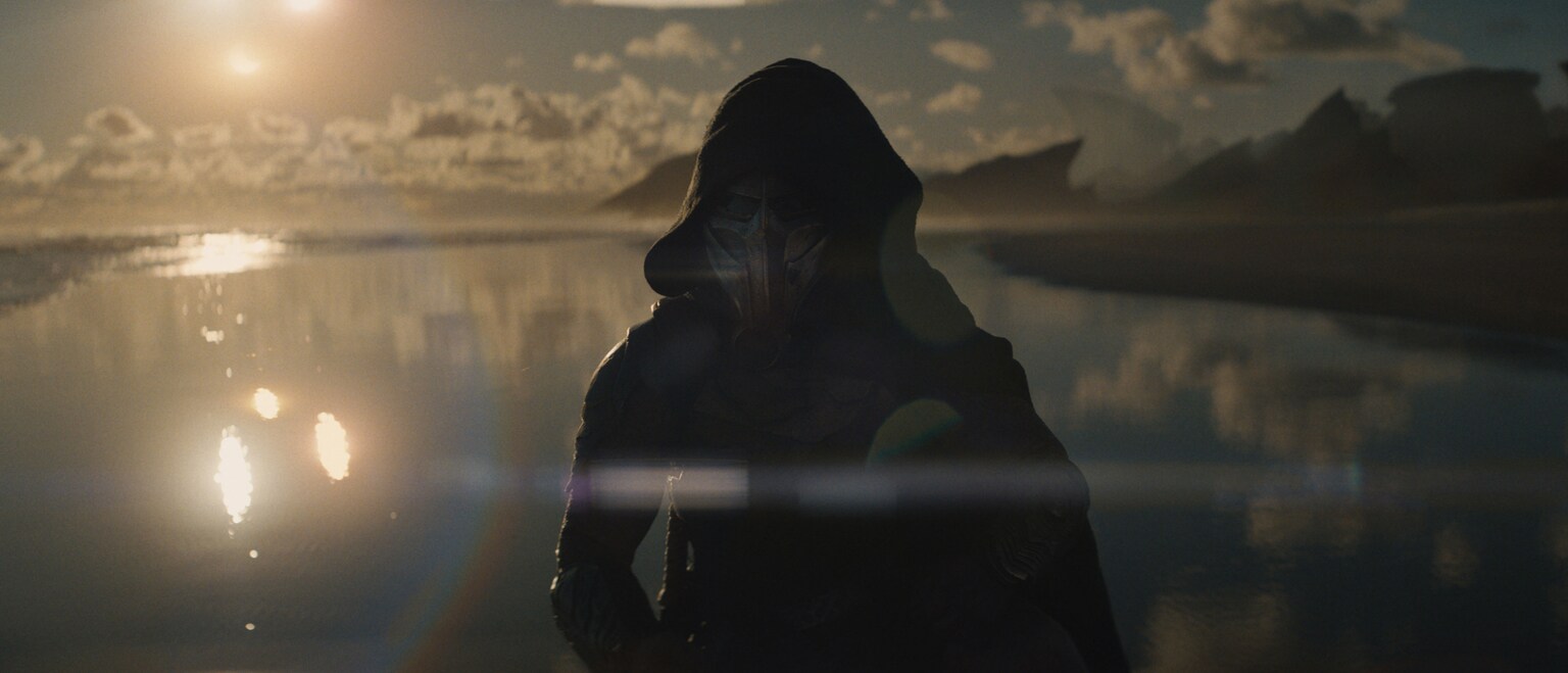 Image of a predator wearing a hooded robe in front of a large body of water from the 20th Century Studios movie, "Predator: Badlands."