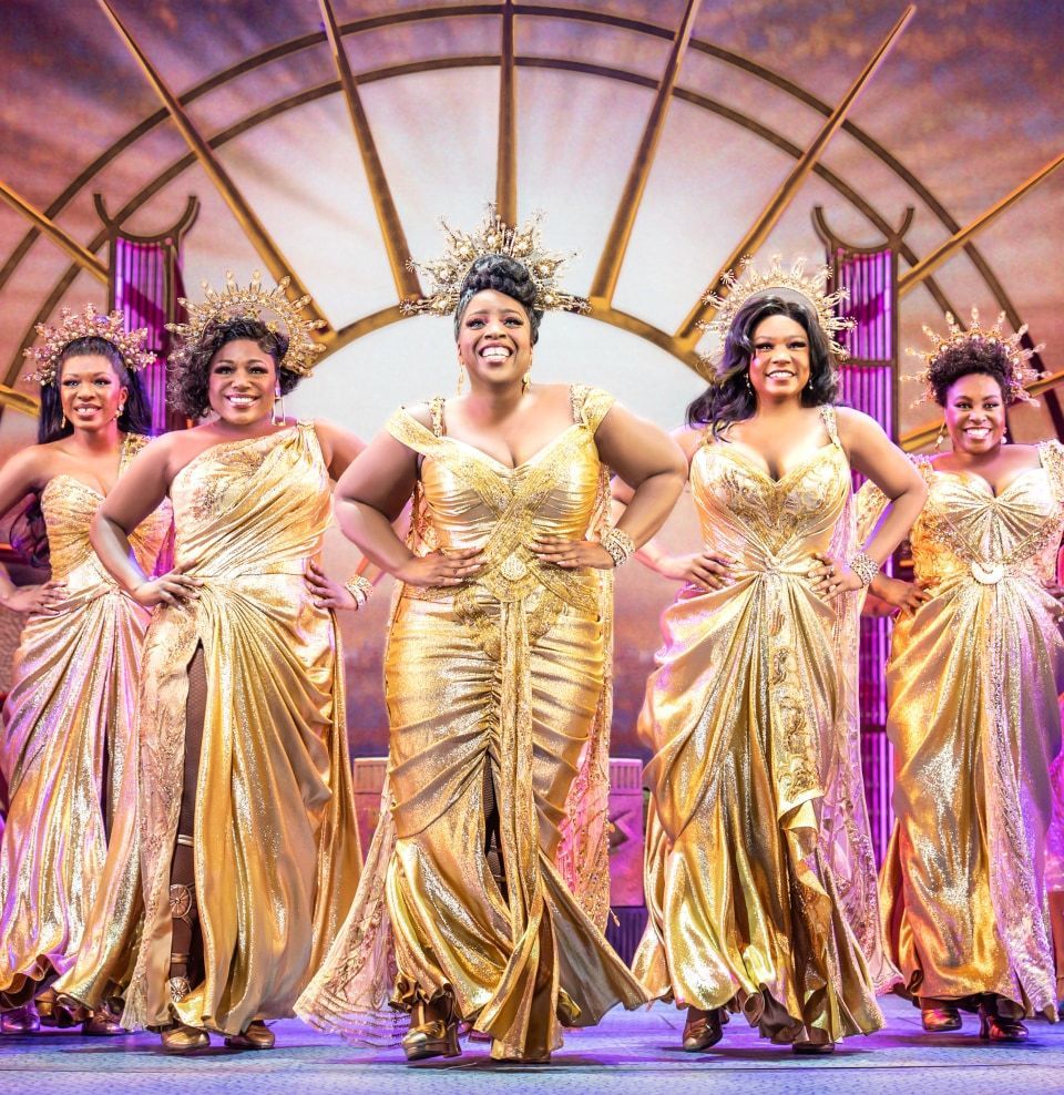 A production shot of the Muses from Hercules in gold dresses and crowns