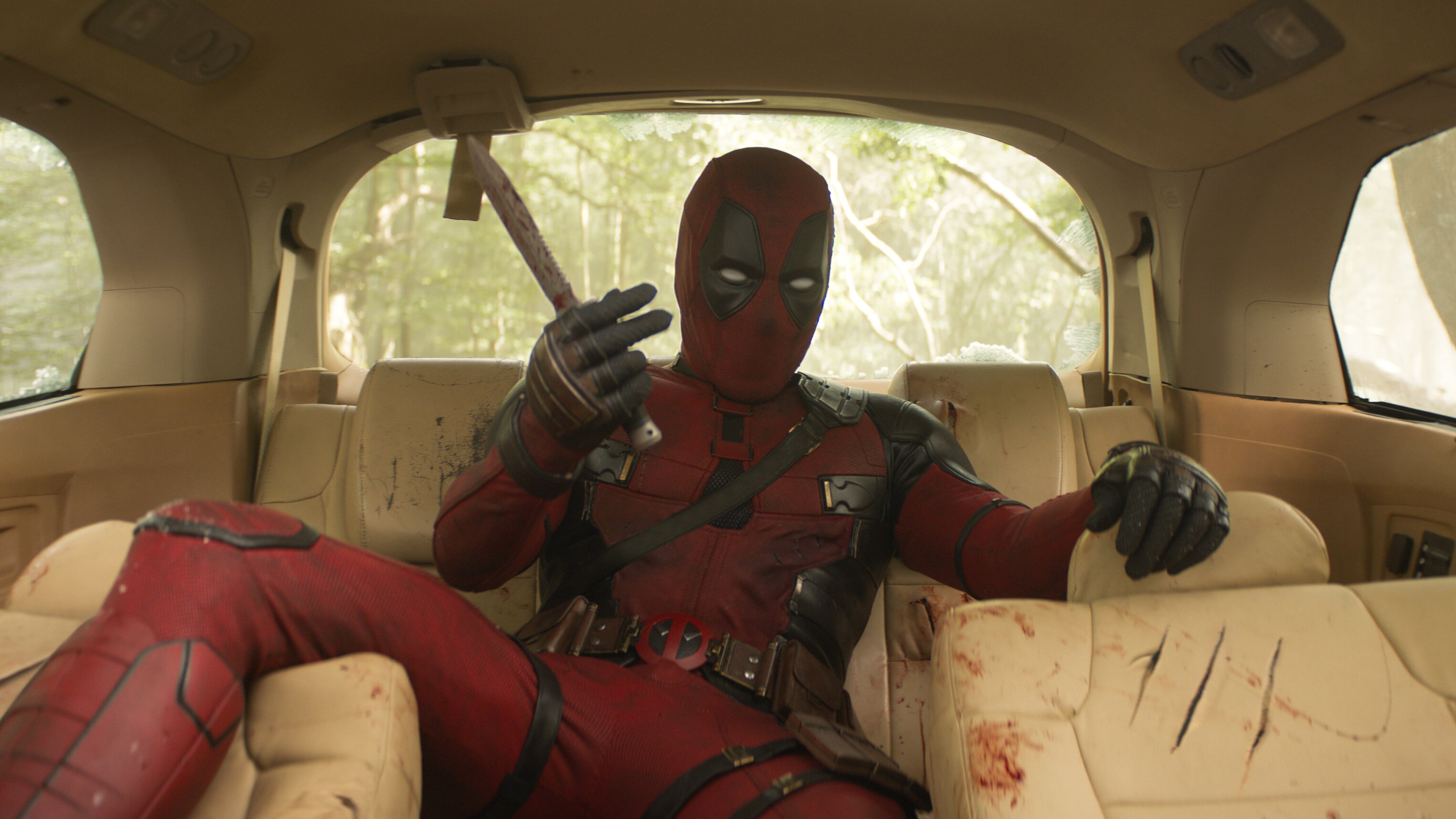 Deadpool aka Wade Wilson (actor Ryan Reynolds) sitting in the backseat of a car holding a weapon from the film "Marvel Studios' Deadpool & Wolverine".
