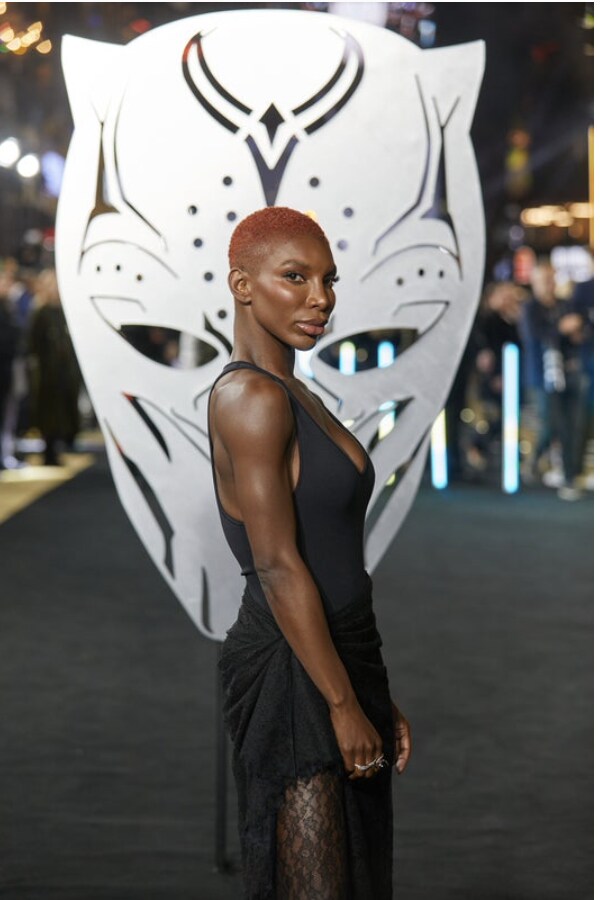 Michaela Coel in front of silver Panther head cut out.