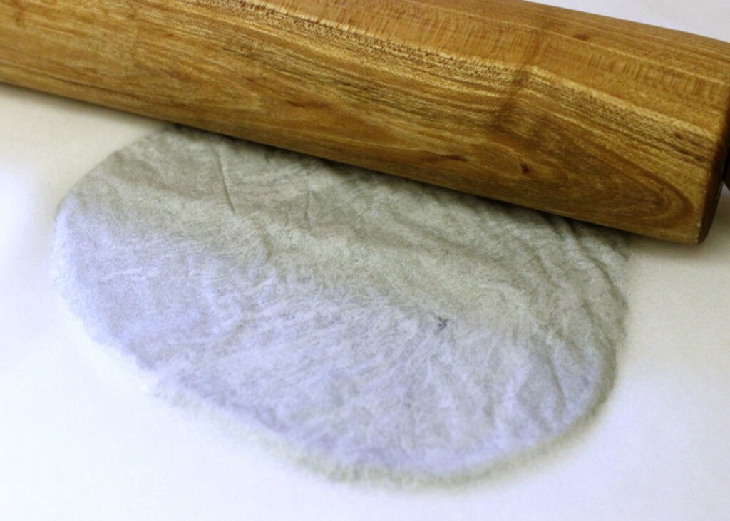 Grey dough, flattened into the shape of a tortilla, and a rolling pin.
