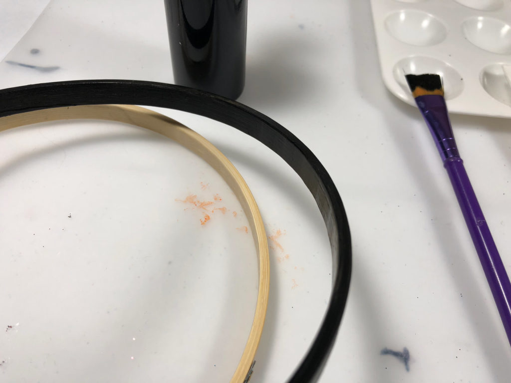 A paintbrush and two embroidery hoops, one painted black, used in the making of homemade droid wind chimes.
