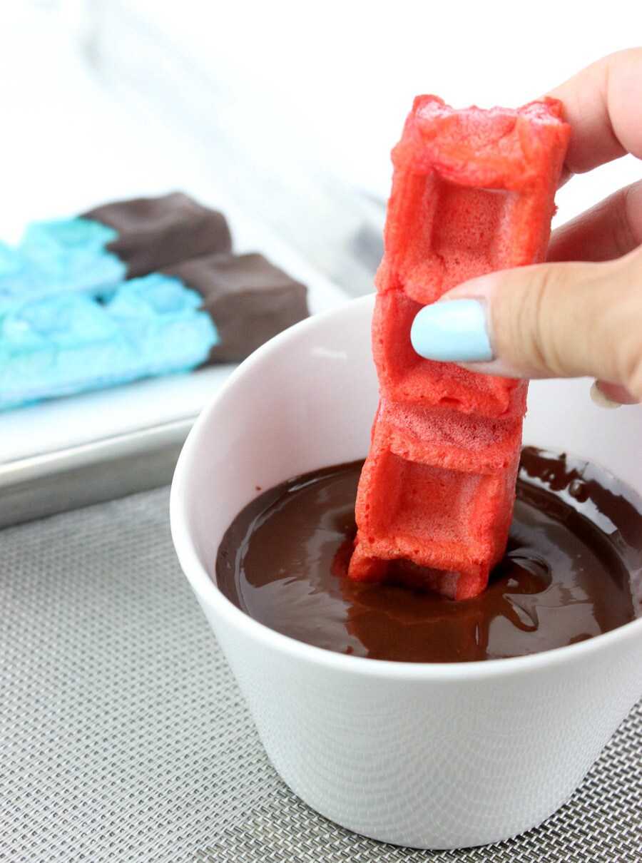 Dipping a red lightsaber waffle stick into melted chocolate.
