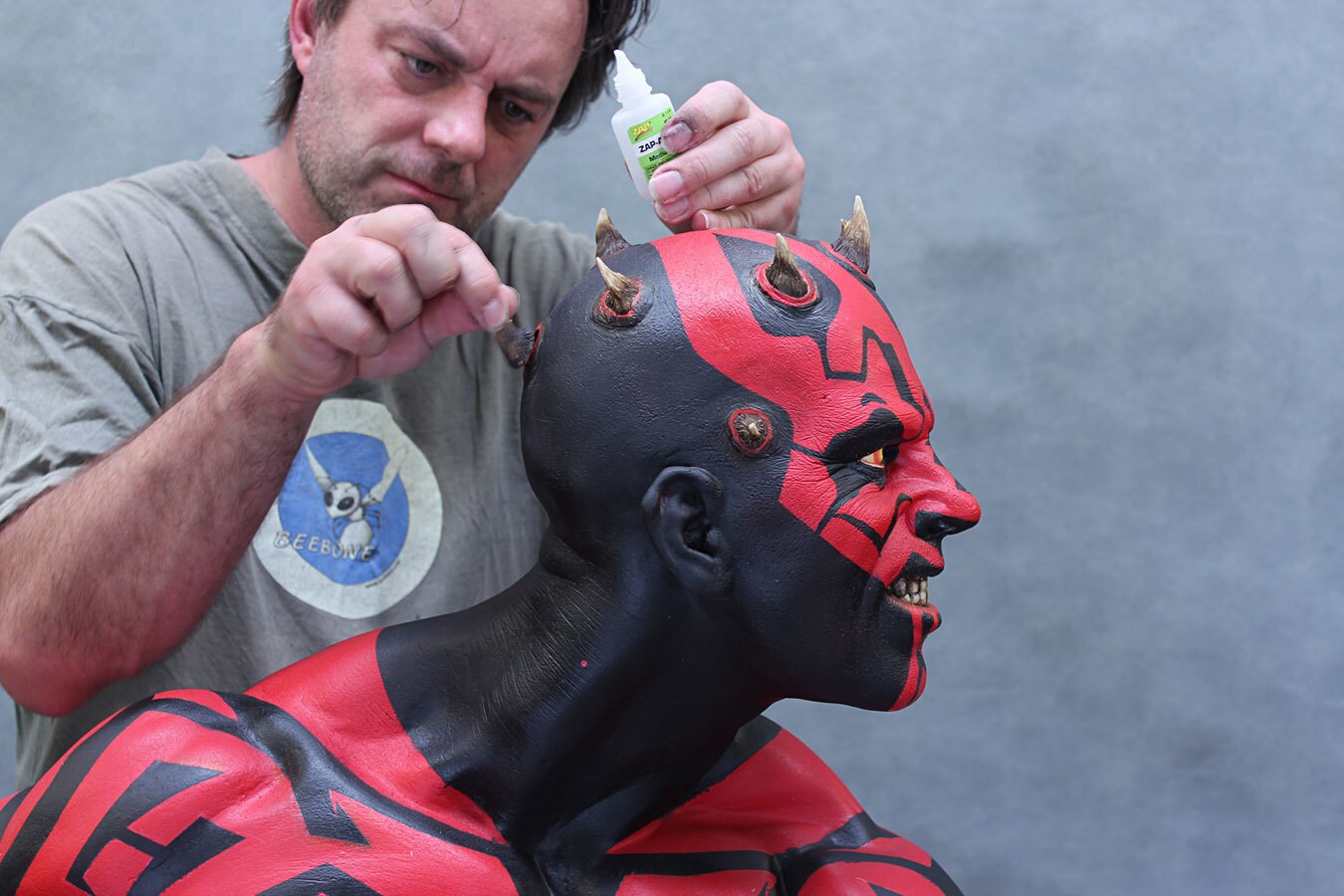 A man glue horns onto a life-sized bust of Darth Maul.