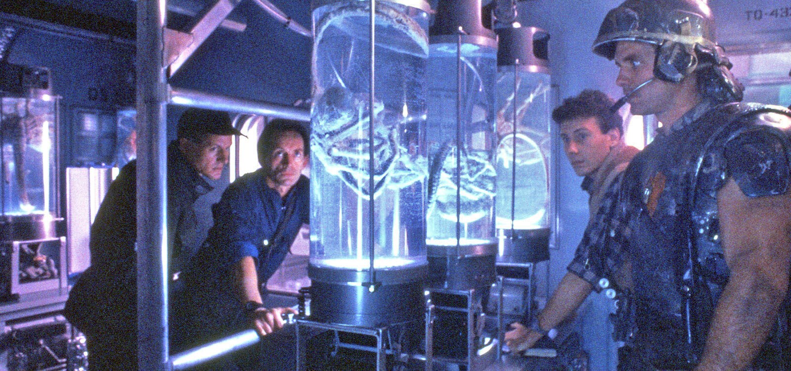 Actors William Hope (as Lieutenant Gorman), Lance Henriksen: Bishop, Paul Reiser (as Burke) and Mark Rolston (as Private Drake) looking at a face hugger alien inside a tube from the movie "Aliens"