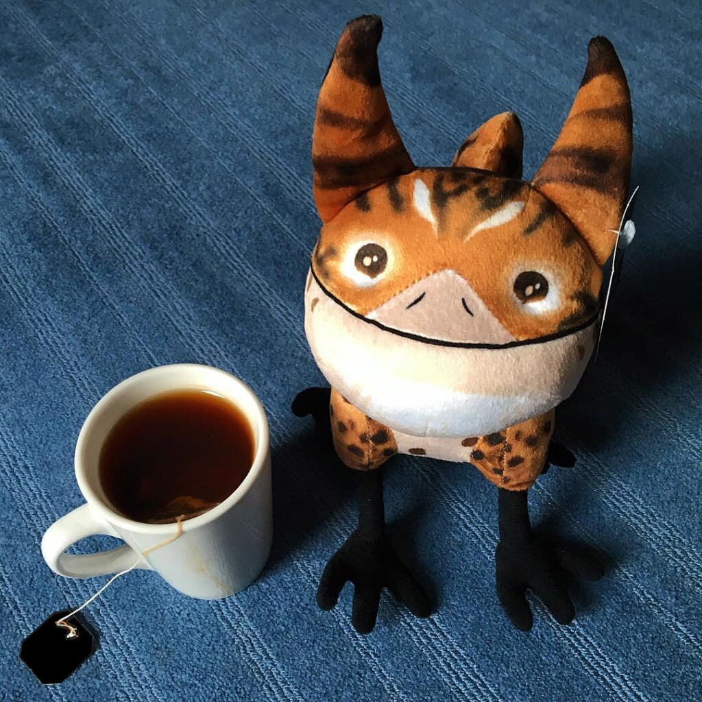 A Loth-cat plush toy stands beside a cup of tea.