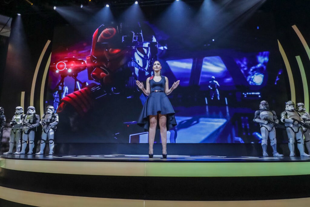 Actor and gamer Janina Gavankar, aka Iden Versio in Star Wars Battlefront II, stands on a stage with stormtroopers.