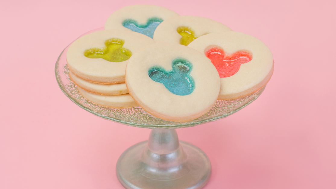 Several round cookies featuring brightly colored Mickey Mouse heads stacked on a cake stand.