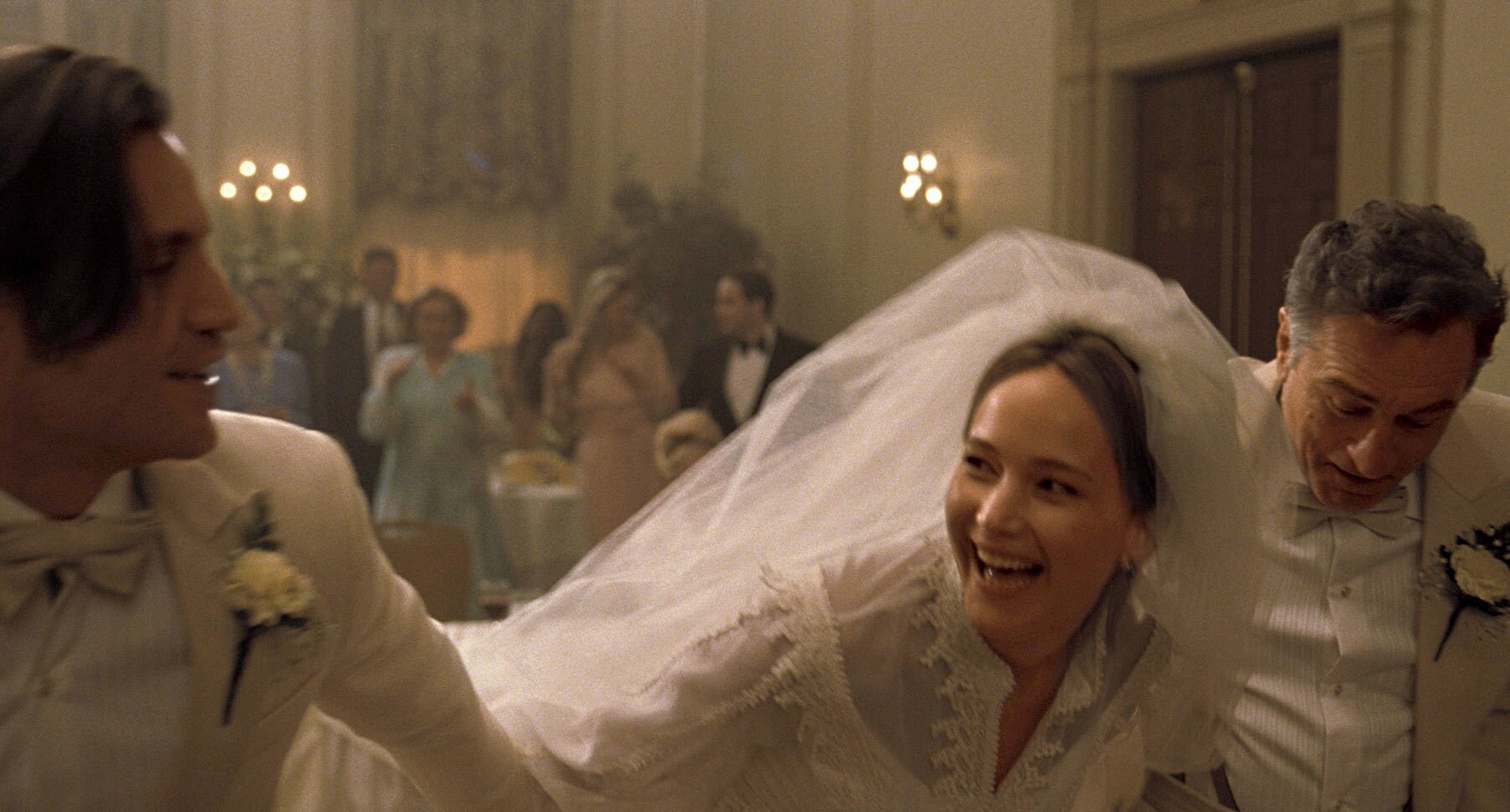 Robert De Niro (as Rudy), Edgar Ramírez (as Tony), and Jennifer Lawrence (as Joy) dancing at a wedding in "Joy"