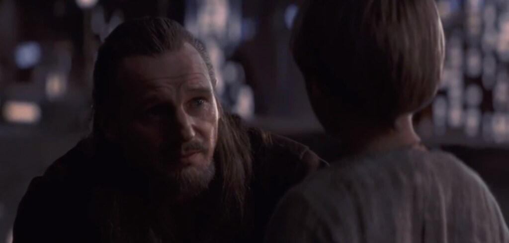 Qui-Gon crouches to speak to a young Anakin.