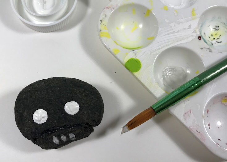 A stone painted to look like K-2SO next to a paintbrush.