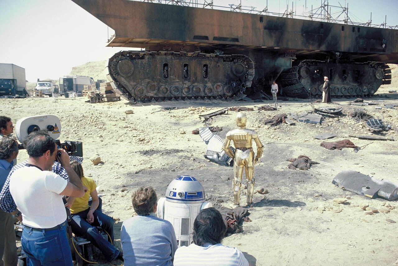 "R2-D2, C-3PO, Luke Skywalker (Mark Hamill), and Obi-Wan Kenobi (Alec Guinness) survey the destruction of Jawas and their sandcrawler on Tatooine."