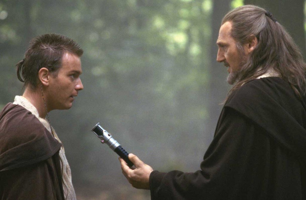 Qui-Gon Jinn hands Obi-Wan Kenobi a lightsaber.