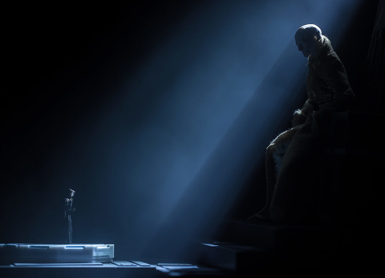 A Snoke action figure sits on a throne while appearing to tower over a Kylo Ren action figure as a light beam breaks through the darkness, partially illuminating both of them. The image comes from toy photographer Noserain.