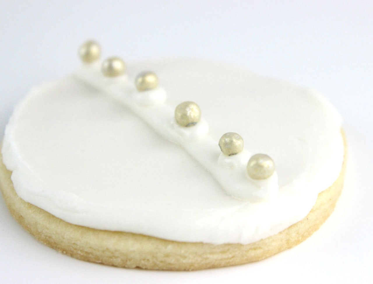 A cookie decorated with white icing and edible silver pearls.