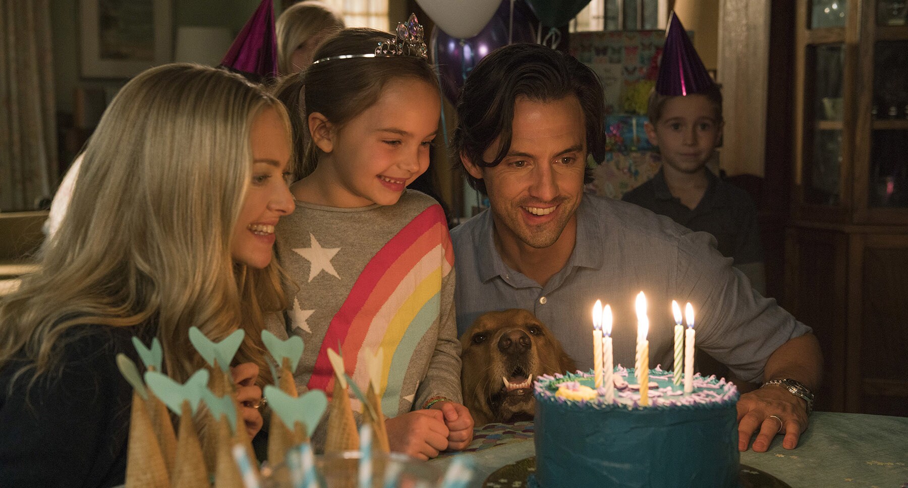 Denny (Milo Ventimiglia), Eve (Amanda Seyfried), dog Enzo and Zoë (Ryan Kiera Armstrong) looking at a birthday cake in the movie "The Art of Racing in the Rain"