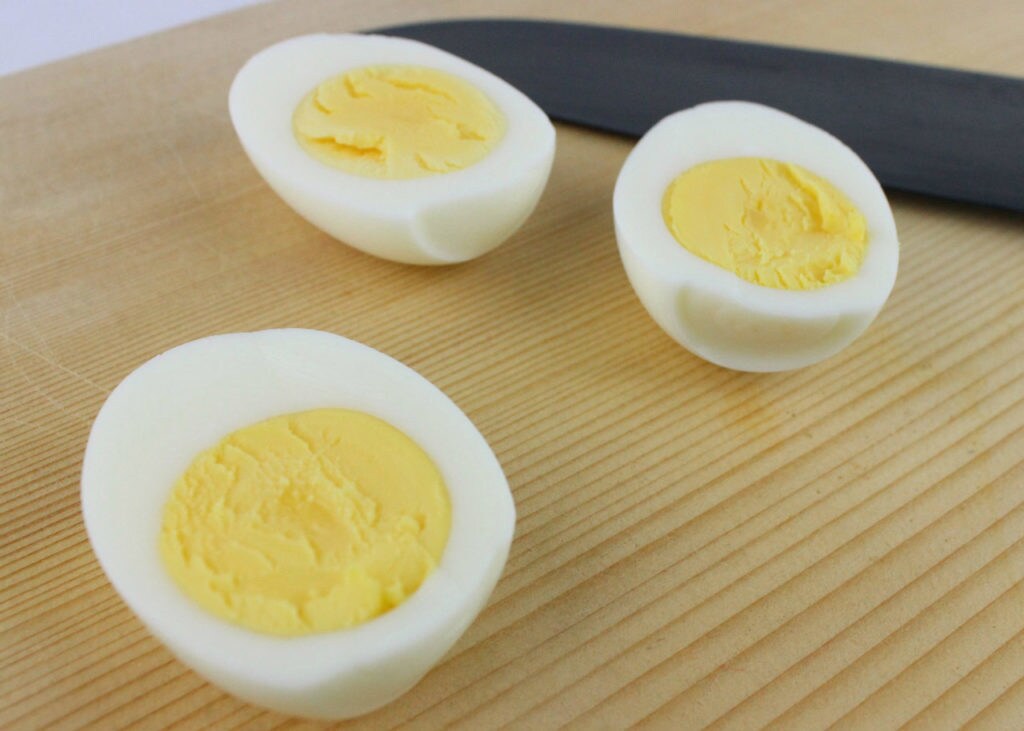 Hard boiled eggs cut into three halves sit on a cutting board next to a knife.