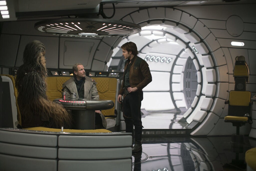 Tobias Beckett, Han Solo, and Chewbacca chat in the lounge area of the Millennium Falcon in Solo: A Star Wars Story.