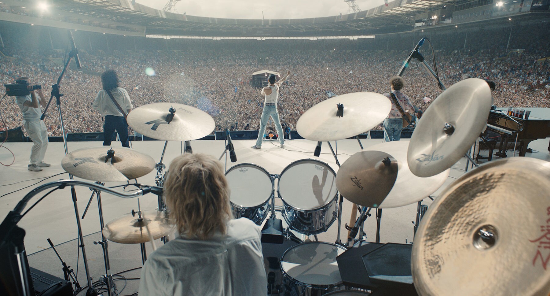 Rami Malek (as Freddie Mercury) Gwilym Lee (as Brian May), Ben Hardy (as Roger Taylor), and Joseph Mazzello (as John Deacon) on large concert stage in front of a large crowd in the movie "Bohemian Rhapsody"