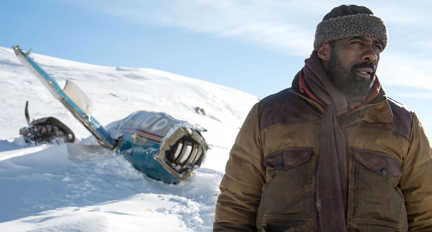 Idris Elba (as Ben Bass) near plane wreckage on a snowy mountain in the movie "The Mountain Between Us"