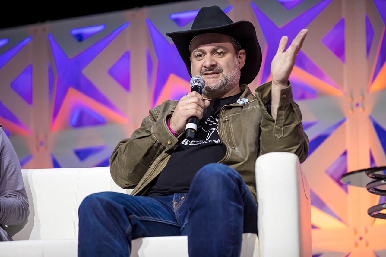 Star Wars Rebels showrunner Dave Filoni sits on a couch while speaking on stage at Star Wars Celebration Chicago.