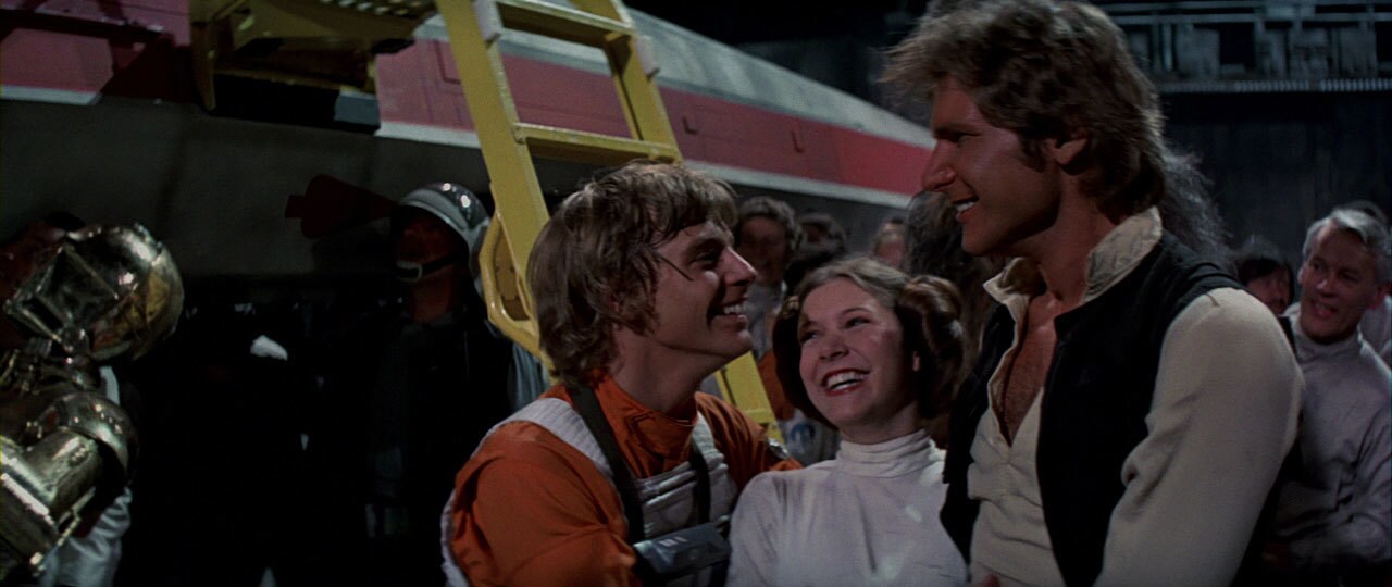 Luke, Leia, and Han laugh and smile in outside of an X-Wing in a Rebel base.