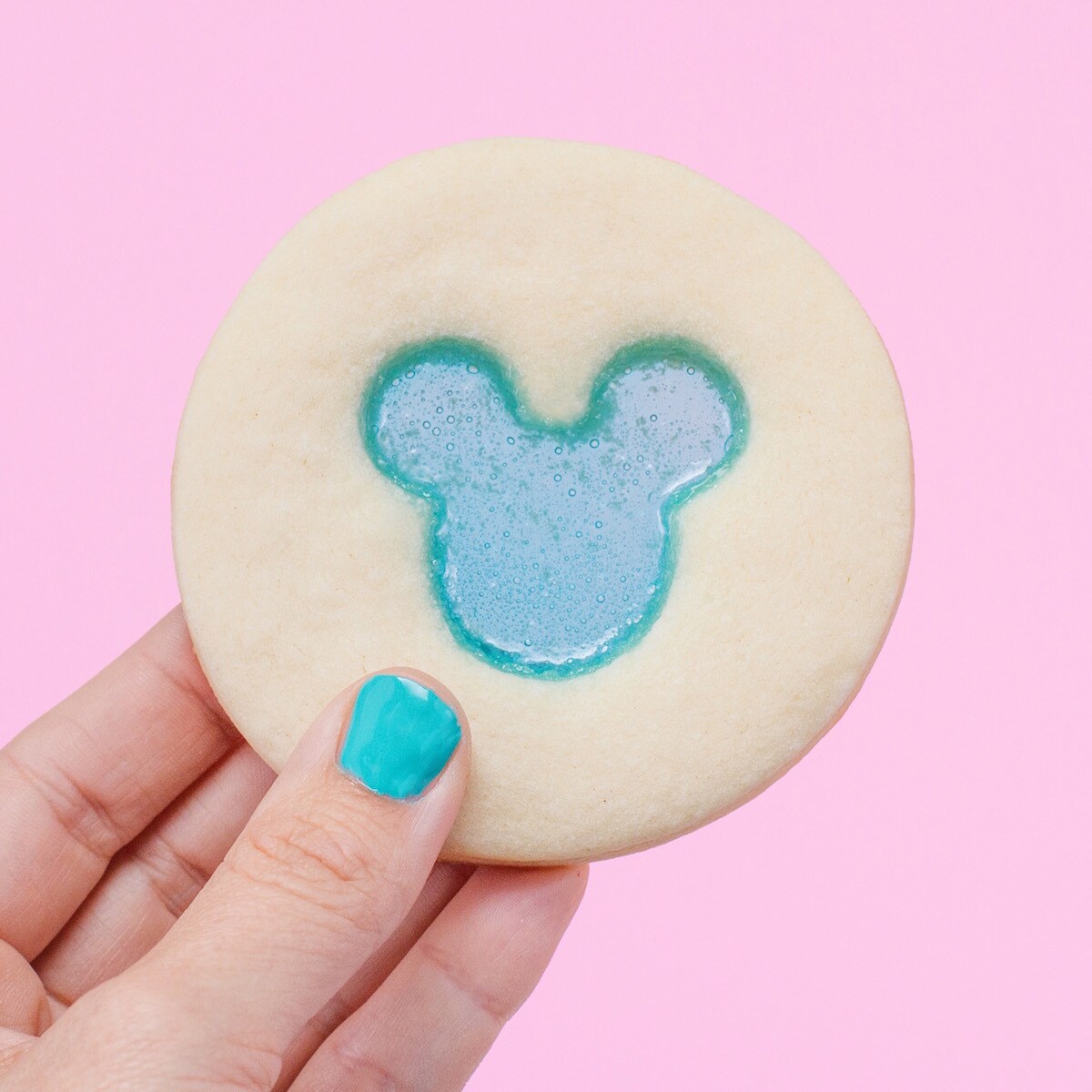 A hand holds up a cookie with a translucent blue Mickey Mouse head in the center.