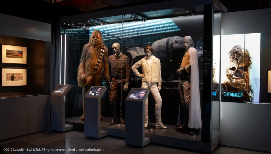 Costumes worn by Han Solo and Princess Leia, next to a life size Chewbacca costume, on display at Star Wars Identities.