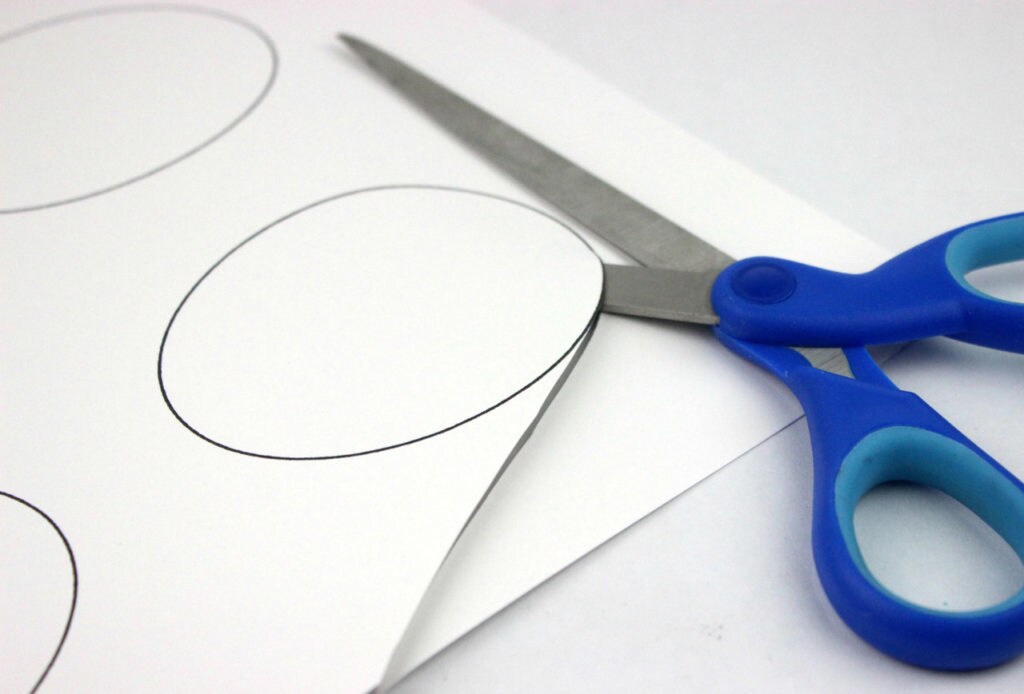 Scissors cut an oval out of paper using a template.